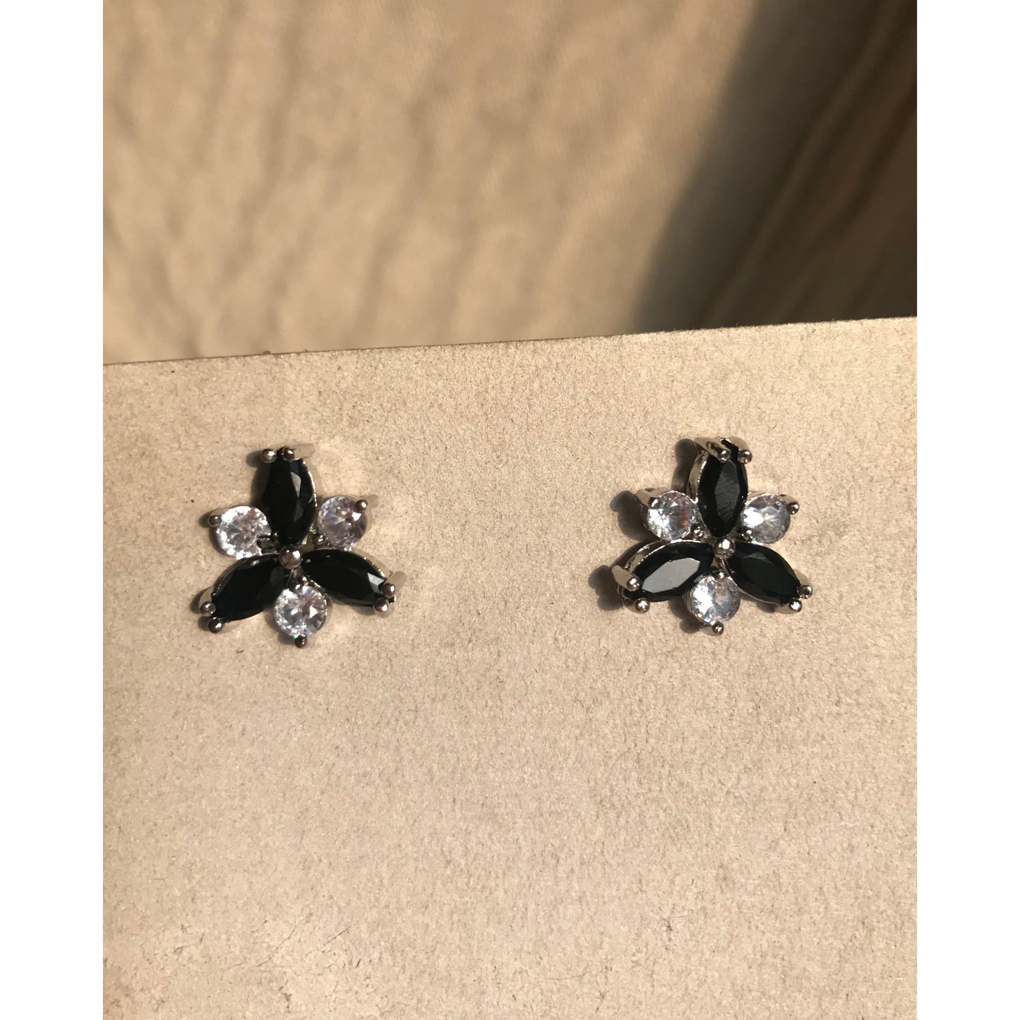 Pair of black and clear flower-shaped earrings on a beige surface