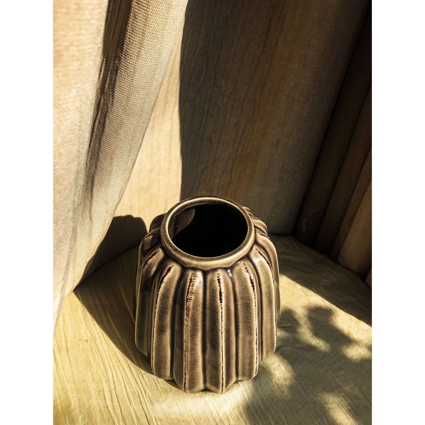 A grey ceramic vase with vertical fluting and a crackled glaze, shown empty and with dried branches inside.