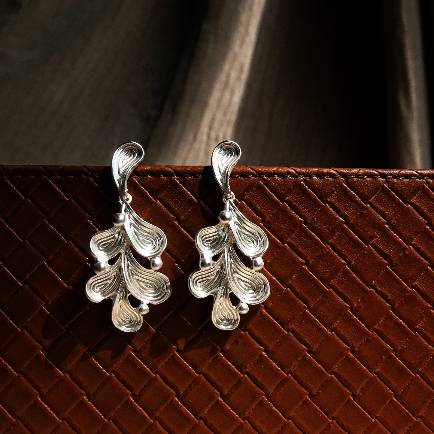 Two abstract drop earrings with swirling lines and small round accents, shown in silver, gold, rose gold, and black variations.