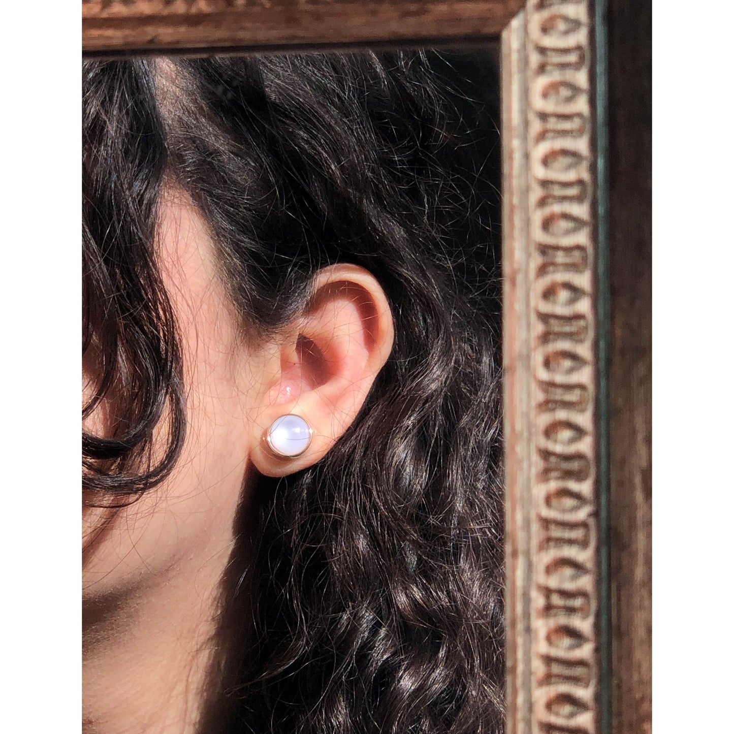 A close-up of a golden-tone, ornate round stud earring with intricate filigree patterns