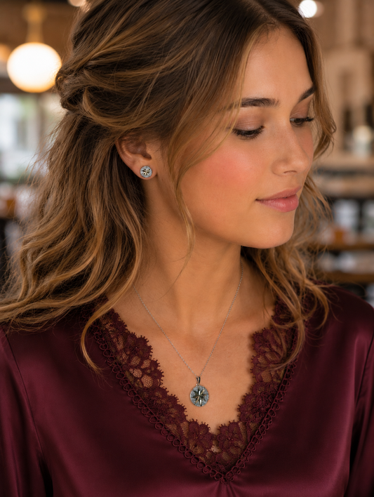 Woman wearing a silver starburst pendant necklace and matching stud earrings with a burgundy satin blouse, showcasing the intricate geometric design and radiant silver finish.