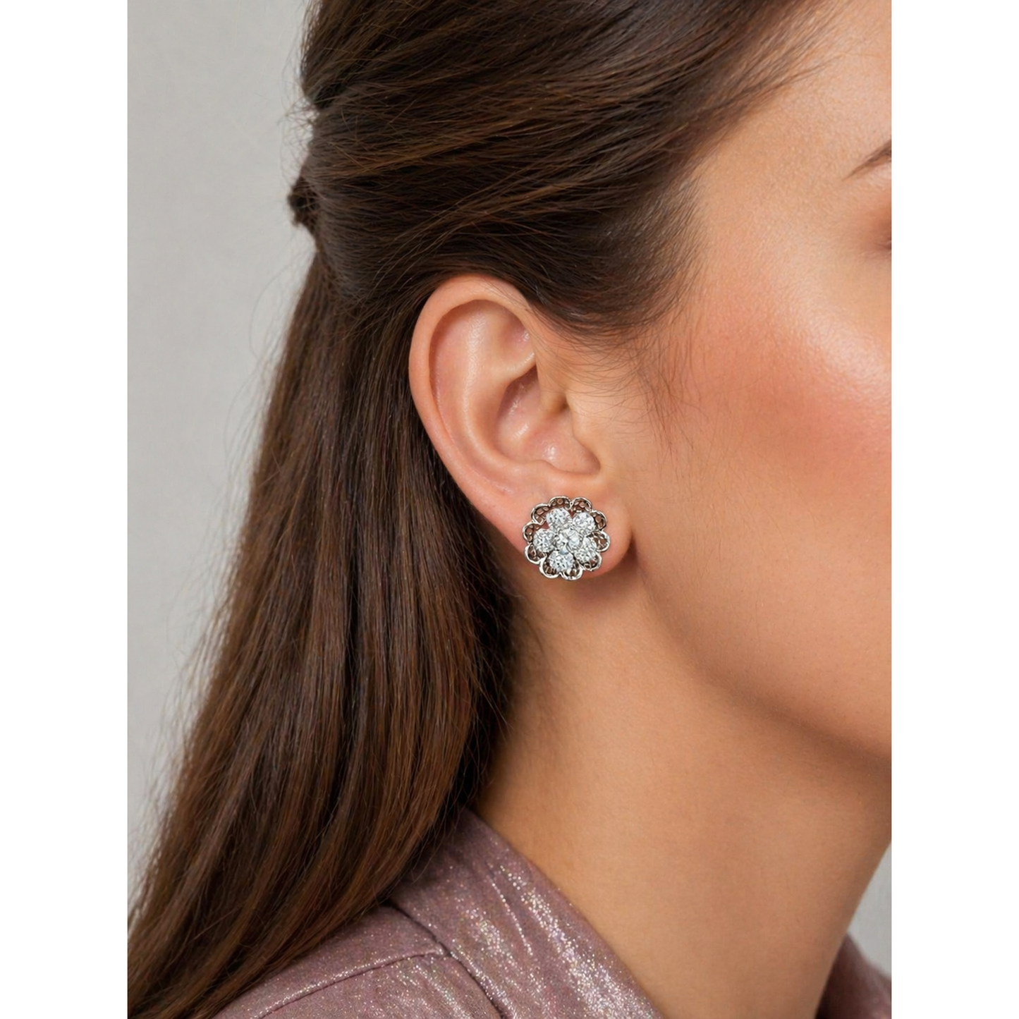 Silver floral crystal stud earrings worn on ear close-up with brown hair and soft makeup highlighting sparkle and detailed design