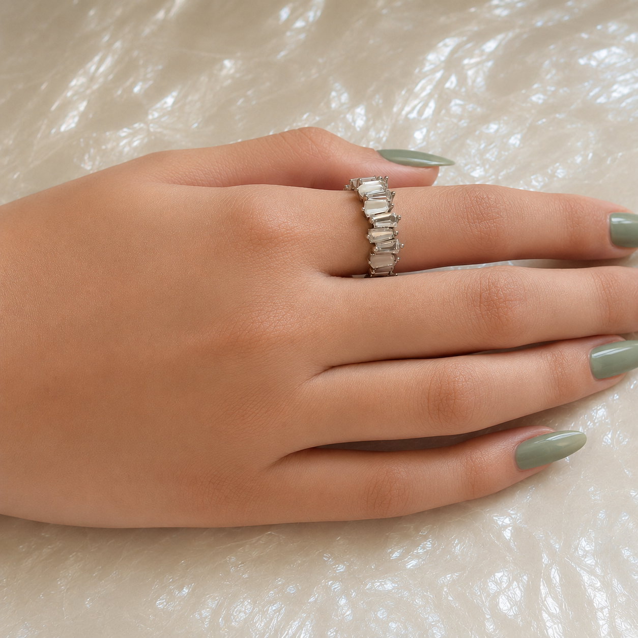 Woman wearing a silver statement ring with natural mother-of-pearl baguette stones on a pearlized surface in a luxury lifestyle setting.