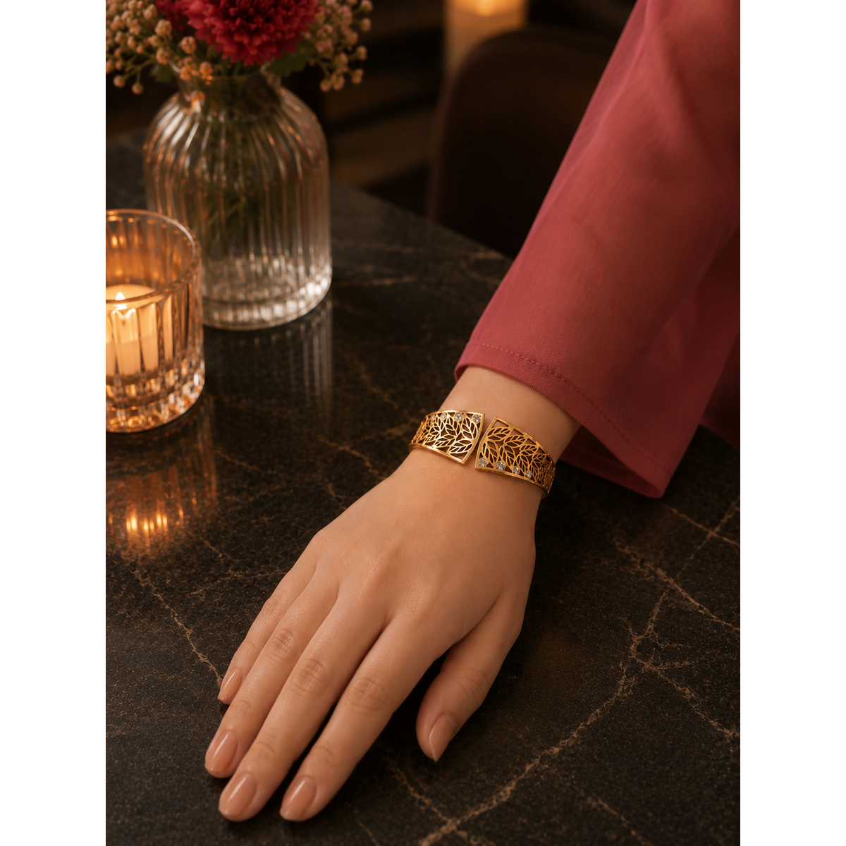 Woman wearing a gold botanical magnetic cuff bracelet with crystal detailing, styled on a luxury restaurant table with warm candlelight and elegant floral décor.