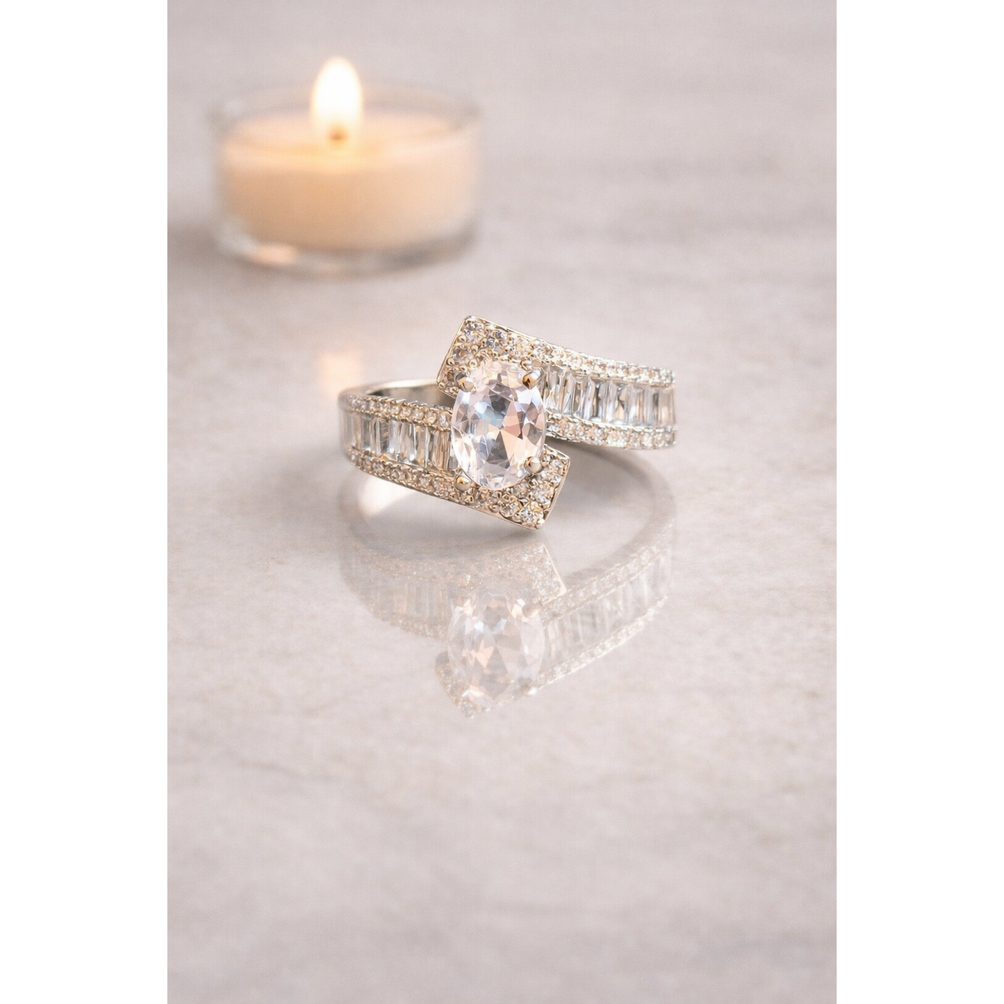 Silver double-band oval center stone ring placed on transparent surface with soft candlelight in background