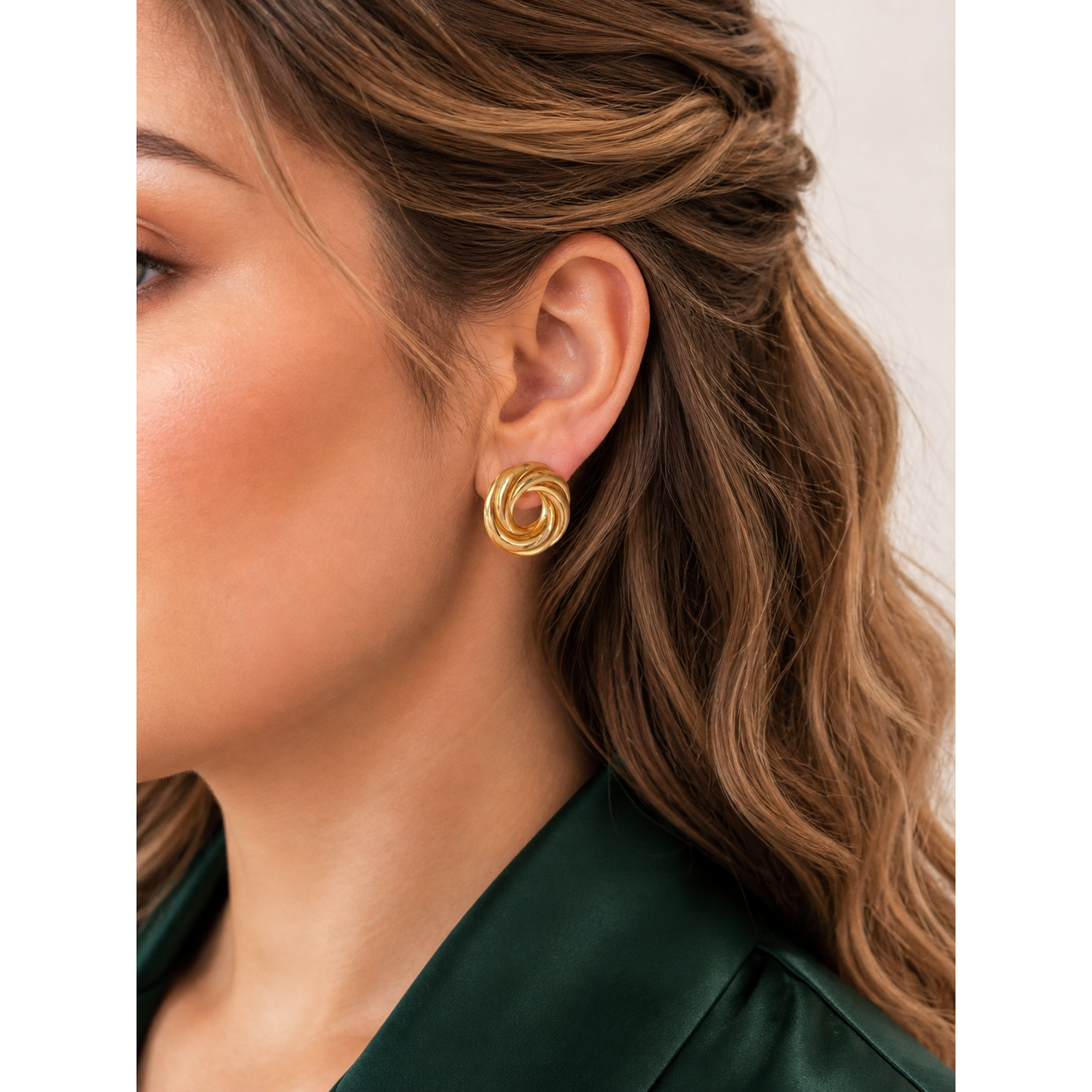 Gold twisted knot stud earrings worn on ear showing swirl design with polished finish