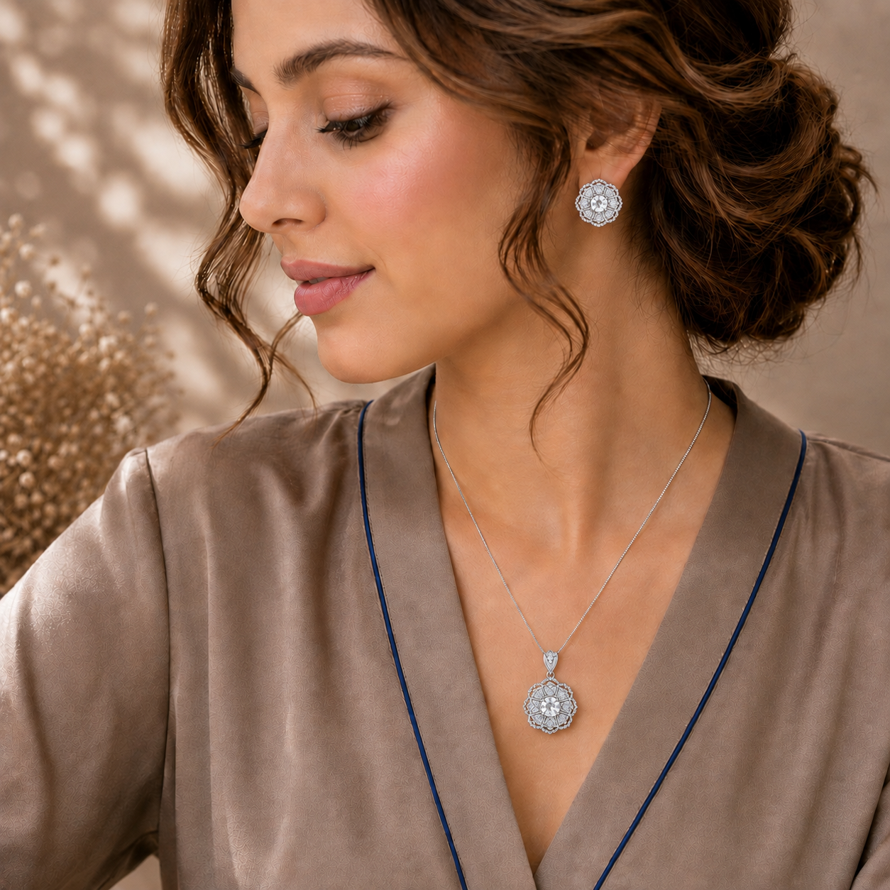 A woman wearing a silver-toned circular pendant necklace and matching earring, styled with a taupe satin robe.