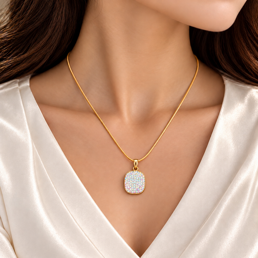 Woman wearing a delicate gold-tone rounded-square pendant adorned with iridescent pastel stones, styled with an ivory satin outfit.