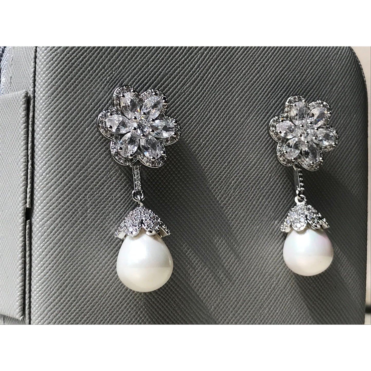Pair of earrings with floral top and pearl drop on a gray textured background