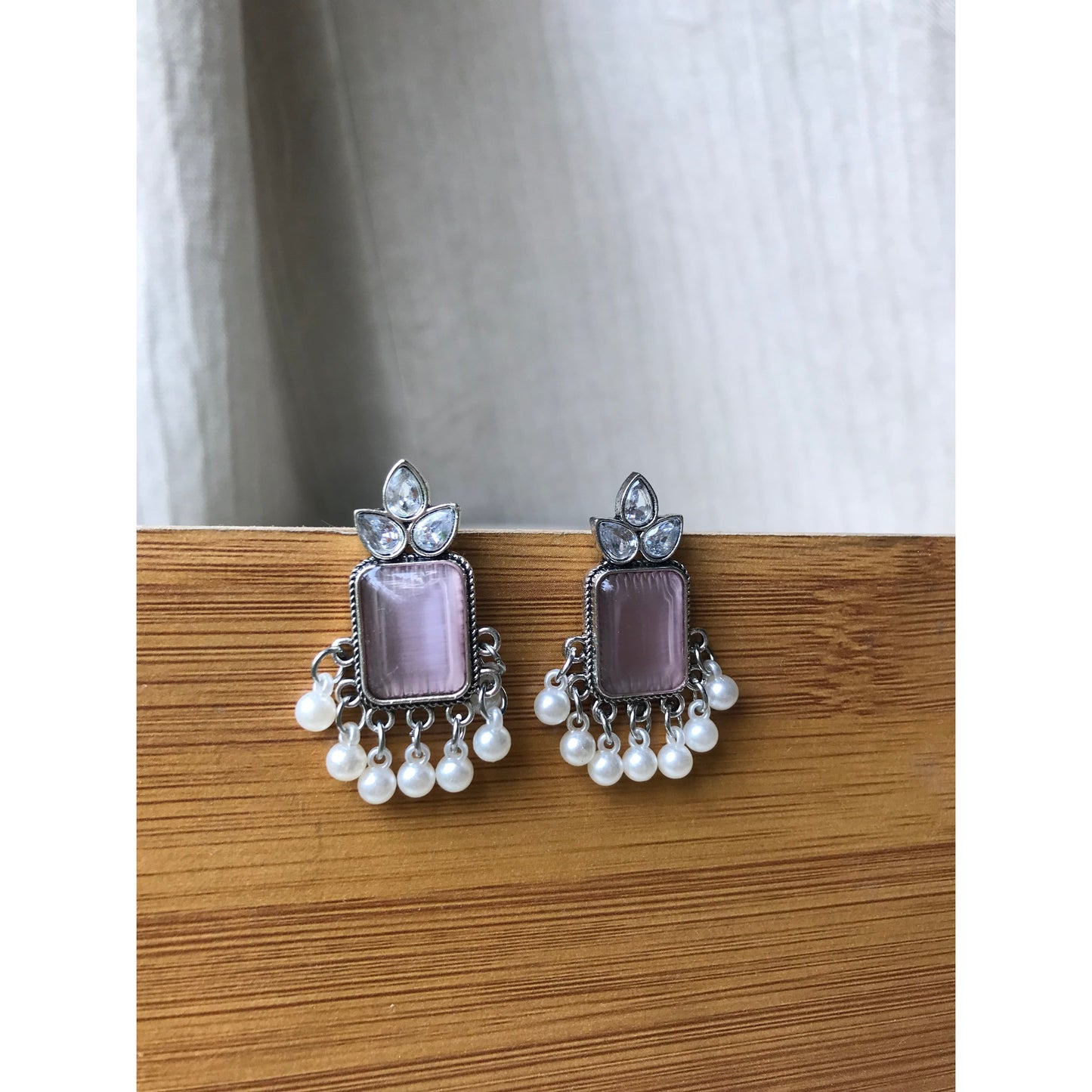 Pair of earrings with pink stones and pearl-like beads on a wooden surface