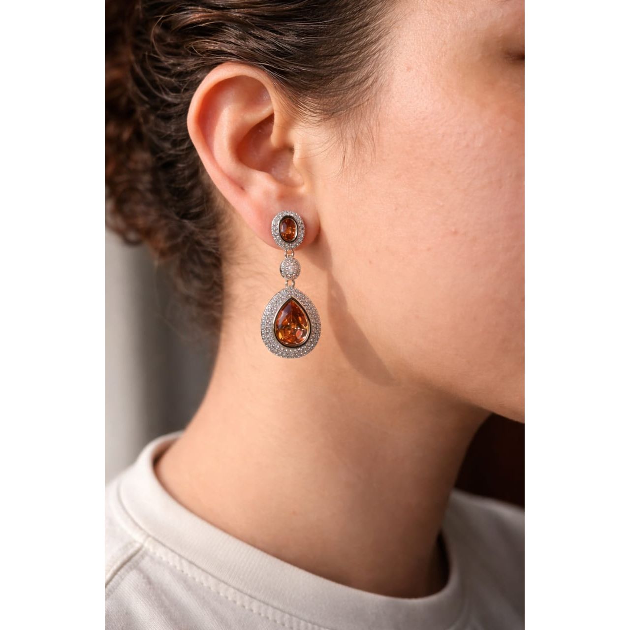 Close-up of a model wearing silver drop earrings with bronze crystal stones, featuring pavé detailing and a contemporary statement jewelry look.