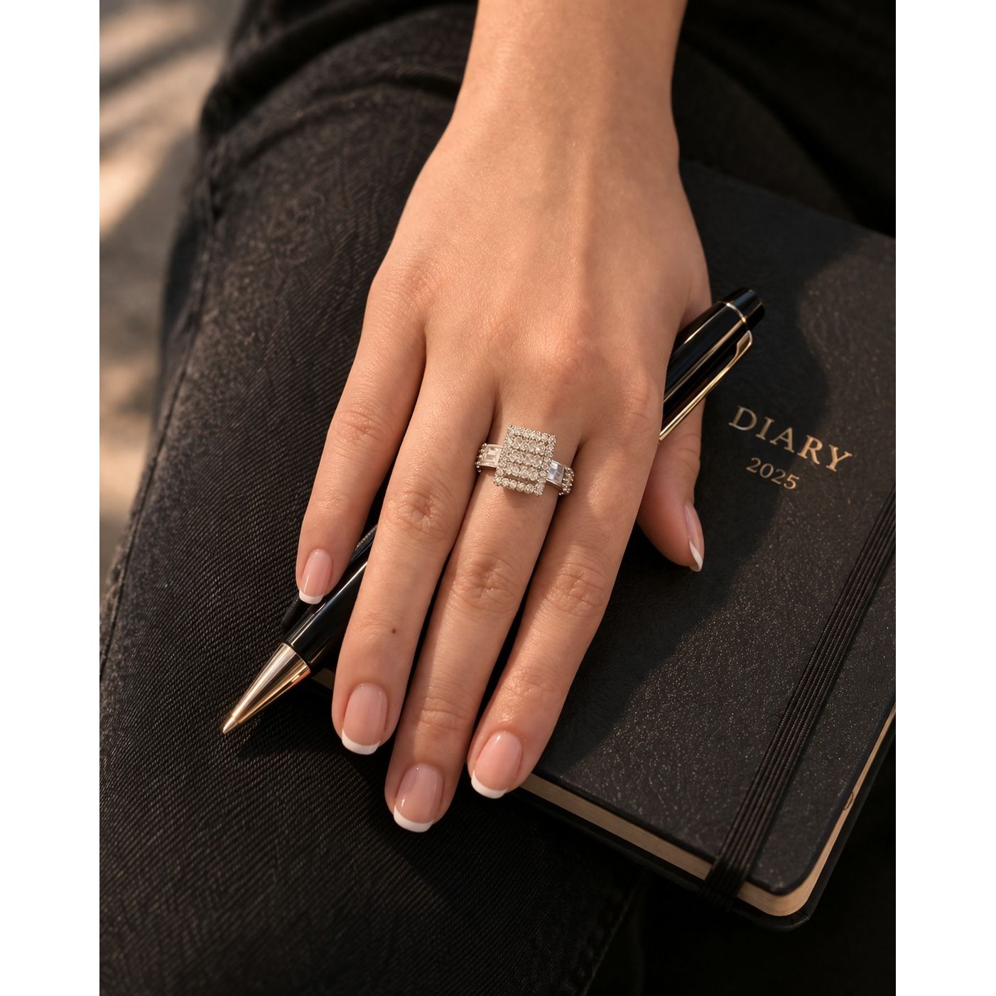 Adjustable crystal cluster ring worn on hand holding black diary and pen with soft natural lighting