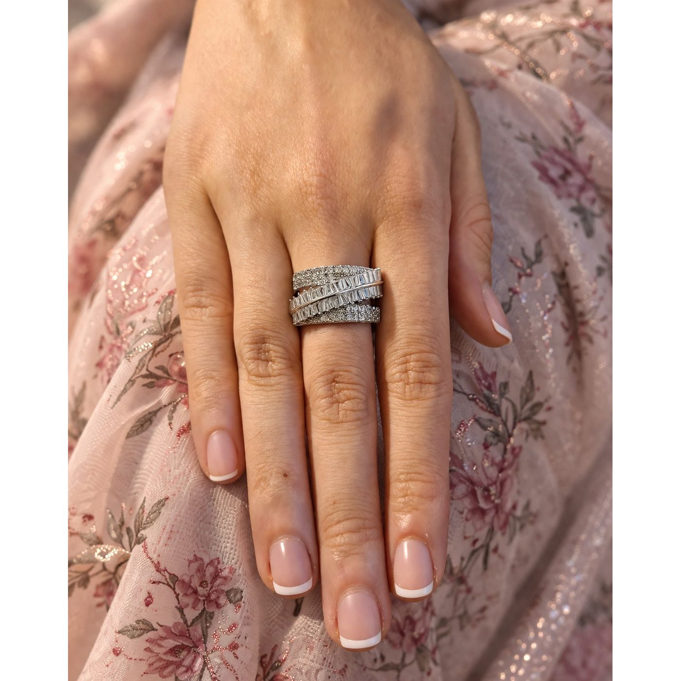 Silver multi layer band ring with baguette and pavé stones worn on hand with soft floral fabric background