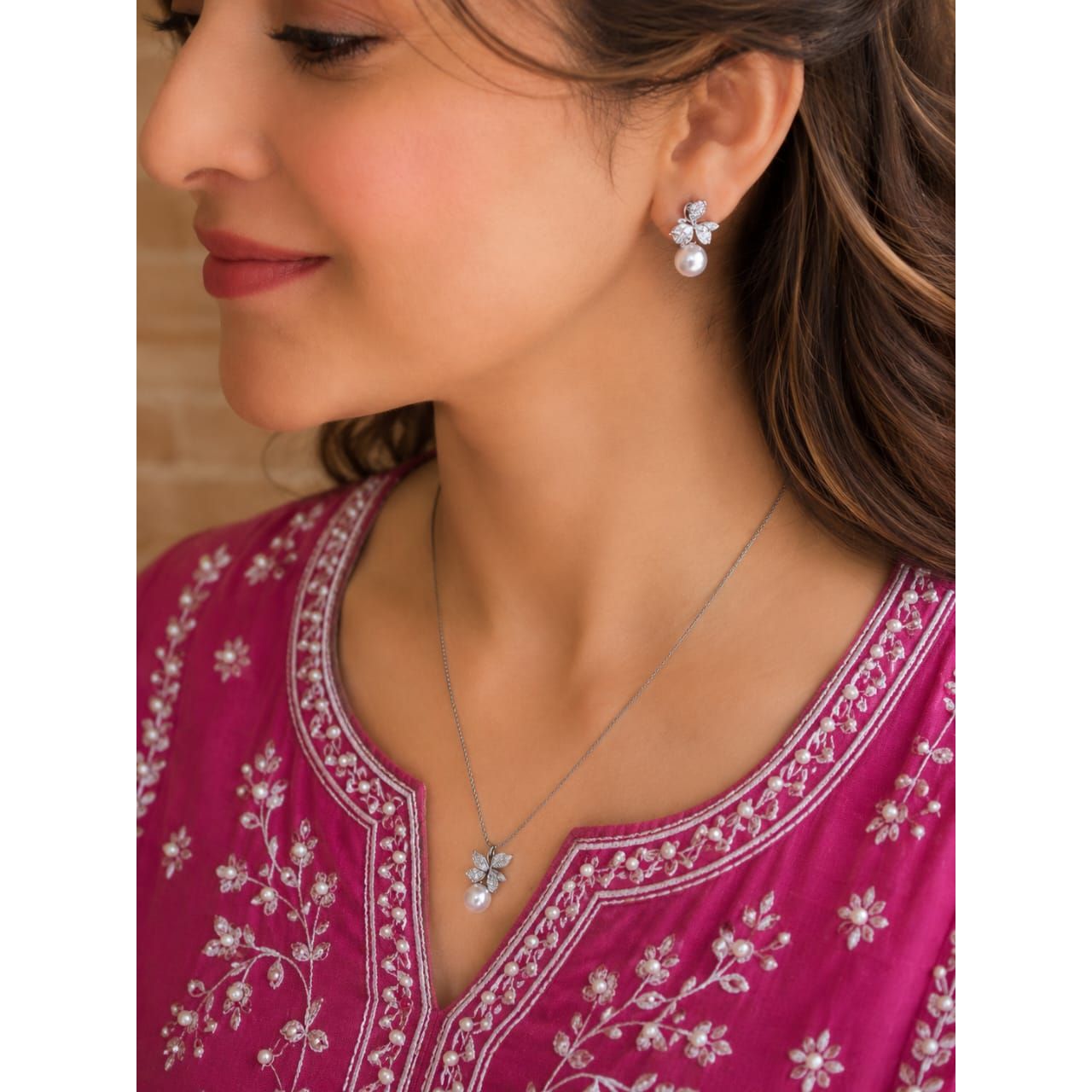 Woman wearing silver crystal flower earrings and matching pearl pendant necklace with bright pink embroidered outfit in a luxury side-profile portrait.