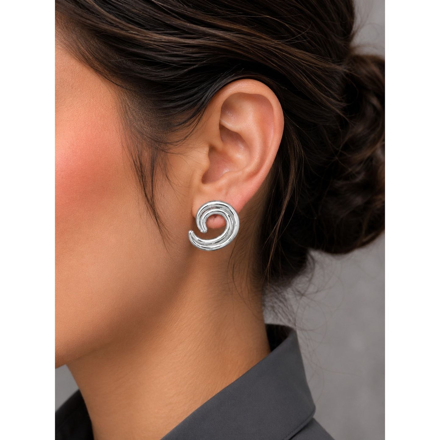 Woman wearing silver spiral statement stud earrings with a modern swirl design and polished metallic finish.