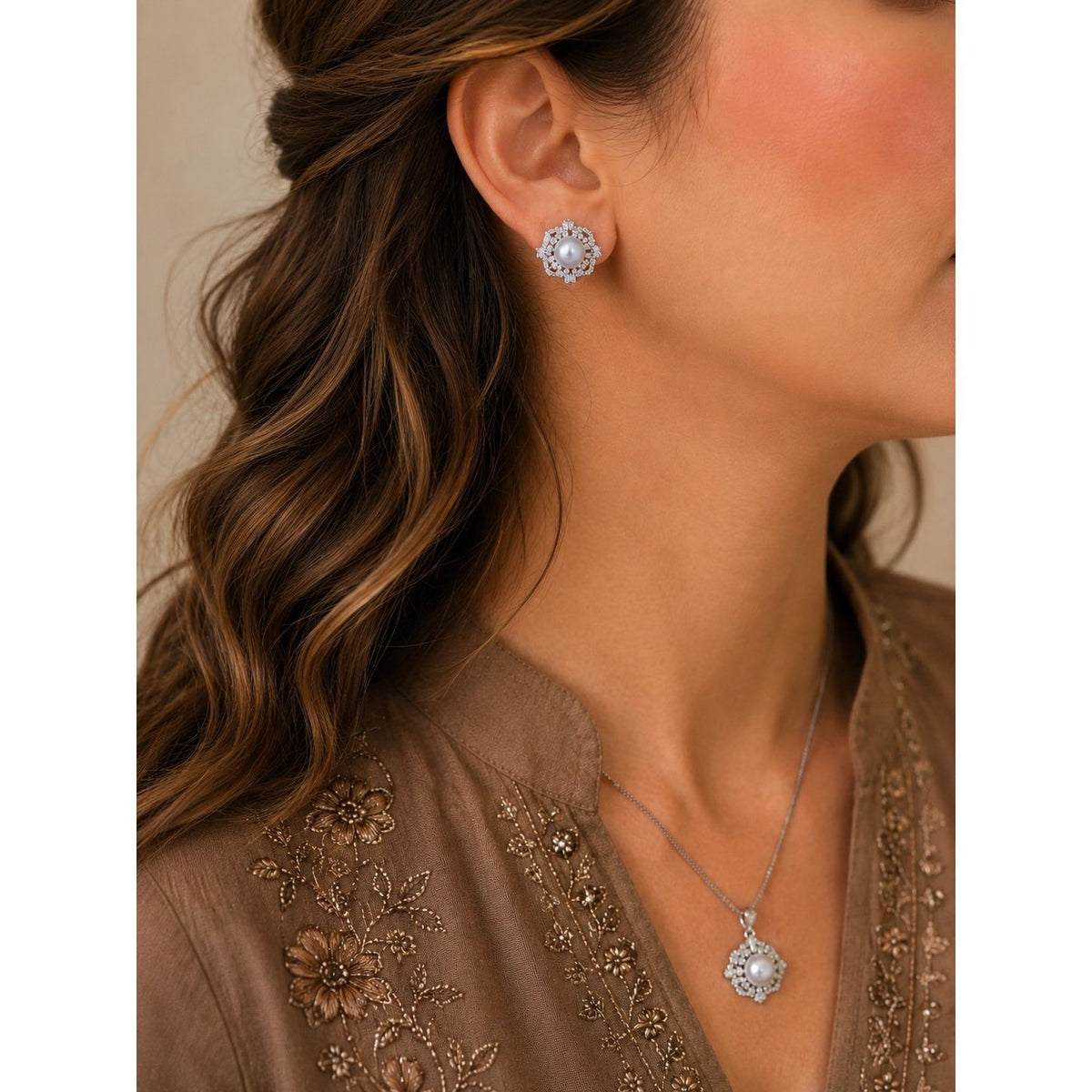 Woman wearing a pearl and crystal floral necklace set with matching stud earrings, styled with a mocha embroidered outfit and soft waves.
