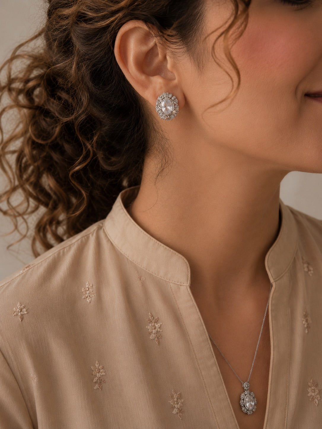 Woman wearing a silver-tone crystal halo necklace and matching oval crystal stud earrings with a soft beige embroidered outfit, showcasing a timeless formal jewelry set.