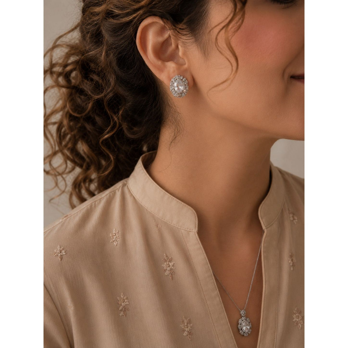 Woman wearing a silver-tone crystal halo necklace and matching oval crystal stud earrings with a soft beige embroidered outfit, showcasing a timeless formal jewelry set.
