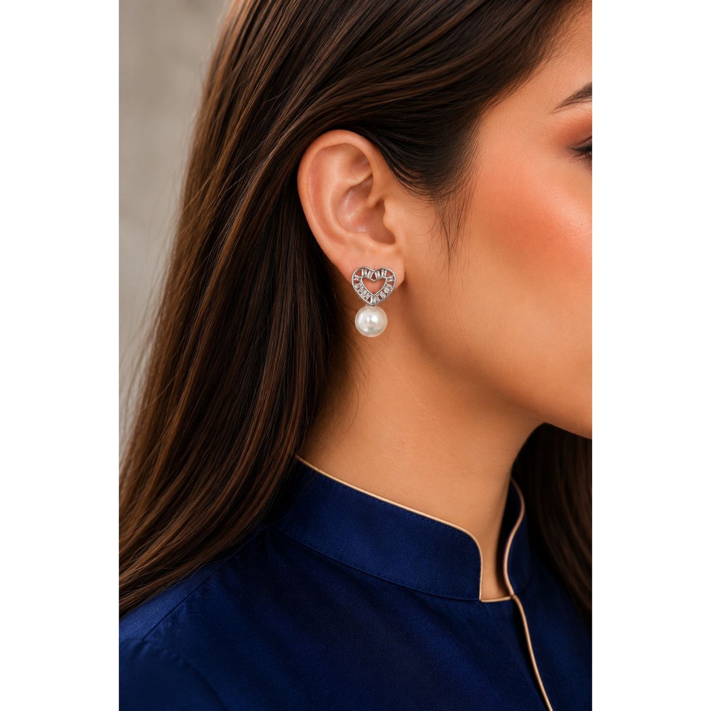 Silver heart-shaped cubic zirconia pearl stud earrings worn by model with navy satin shirt, featuring a lustrous pearl drop.
