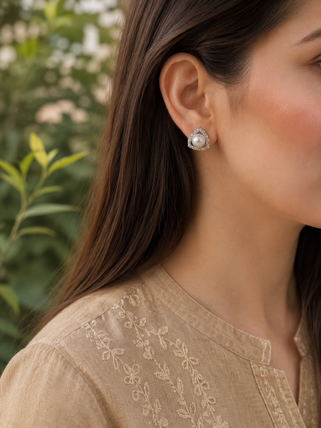 Woman wearing pearl triangle crystal stud earrings with a beige embroidered linen shirt in a close-up portrait.