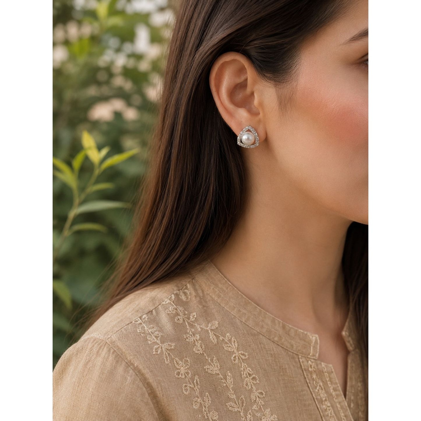 Woman wearing pearl triangle crystal stud earrings with a beige embroidered linen shirt in a close-up portrait.
