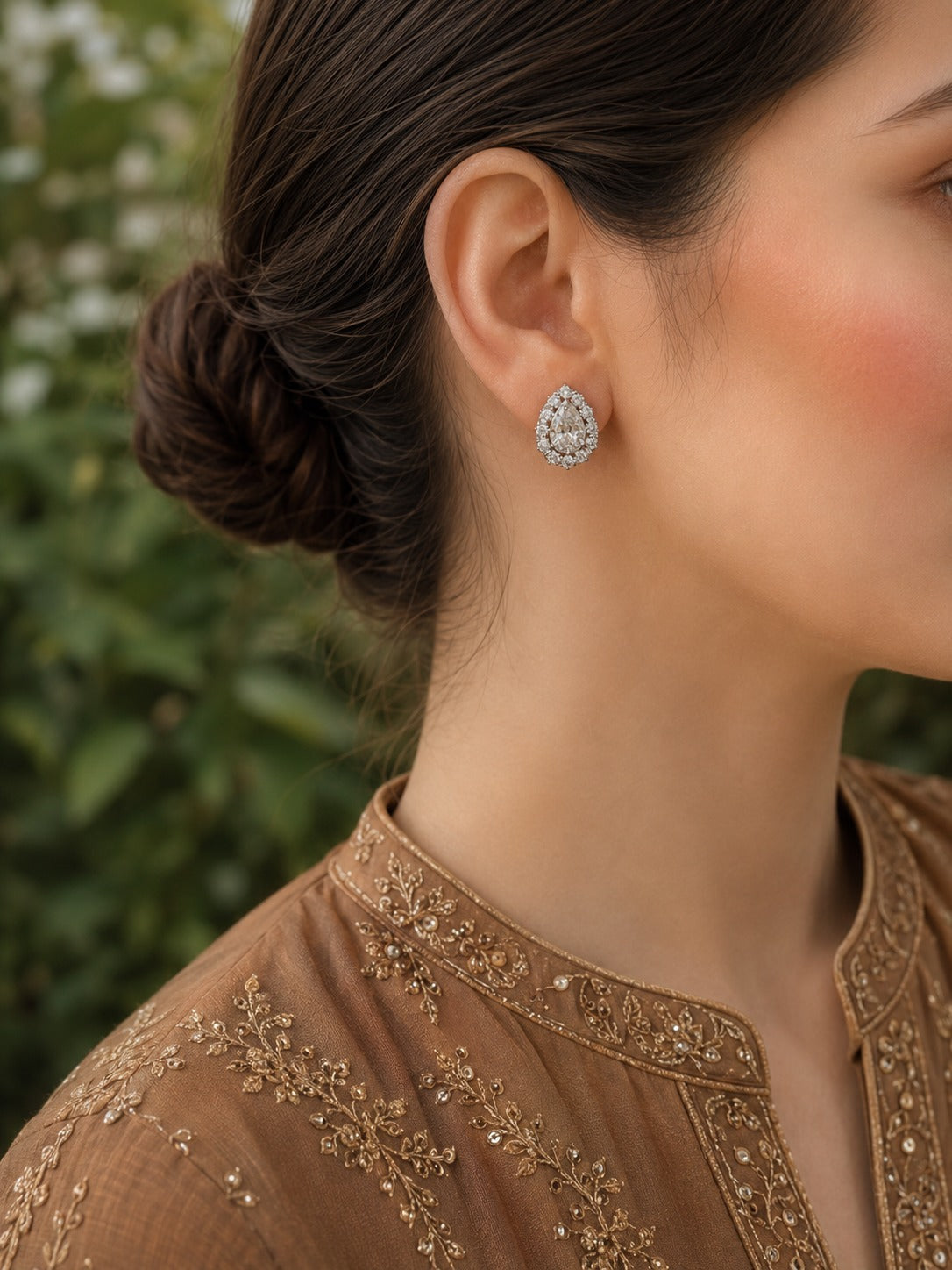 Woman wearing pear-shaped double halo crystal stud earrings with a bronze embroidered linen shirt in a close-up portrait.
