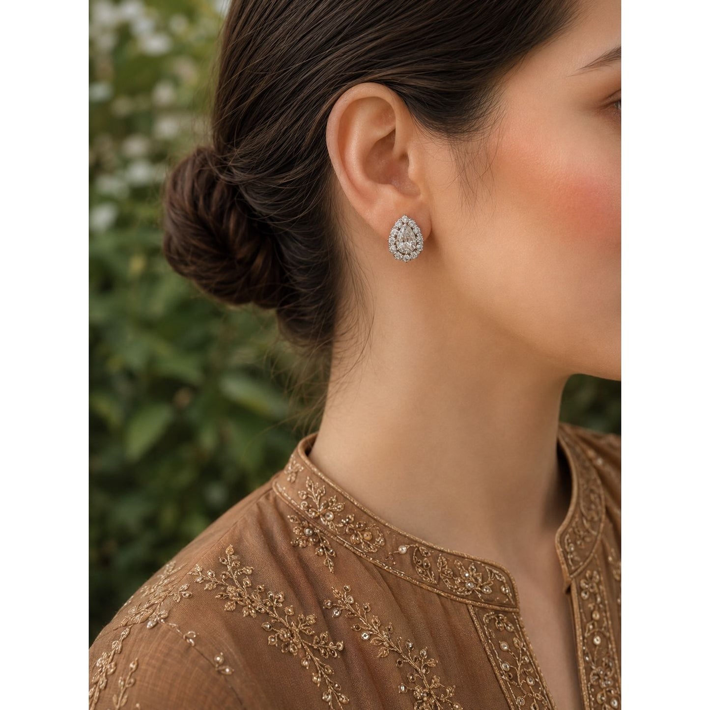 Woman wearing pear-shaped double halo crystal stud earrings with a bronze embroidered linen shirt in a close-up portrait.