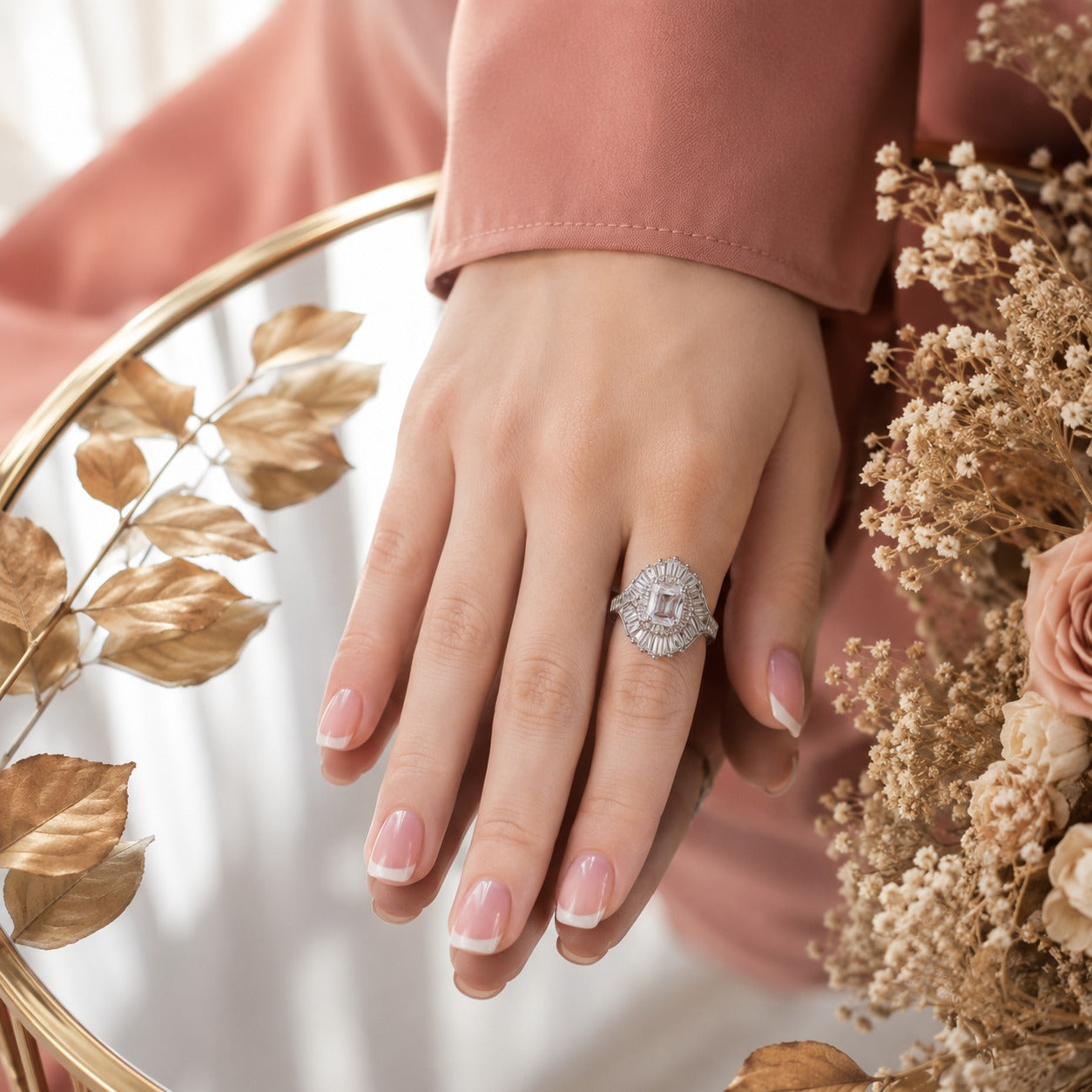 S925 sterling silver radiant halo ring worn on a model's hand with French manicured nails and a soft terracotta satin sleeve.