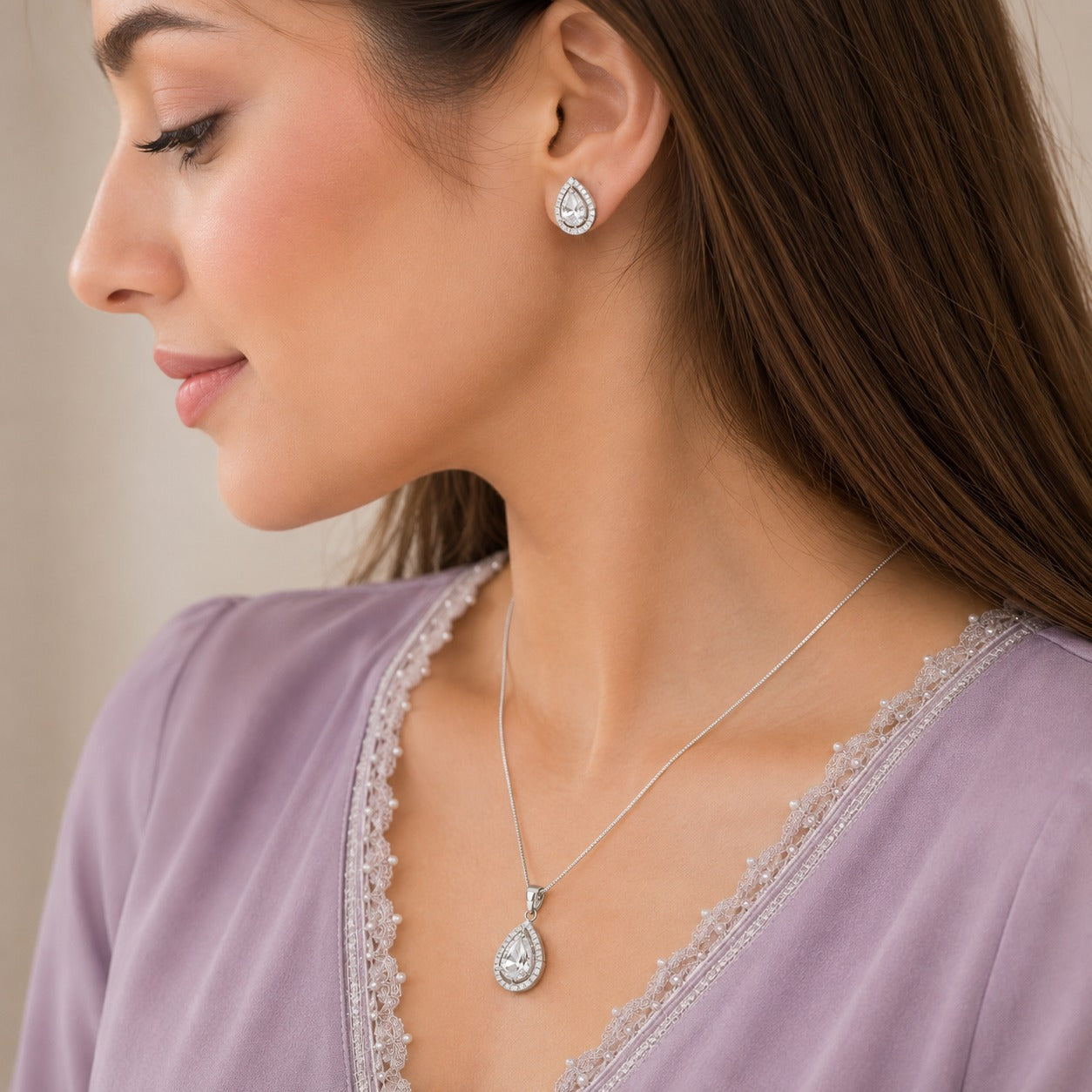 Model wearing a clear zircon teardrop pendant necklace with matching teardrop stud earrings in a polished silver-tone finish.
