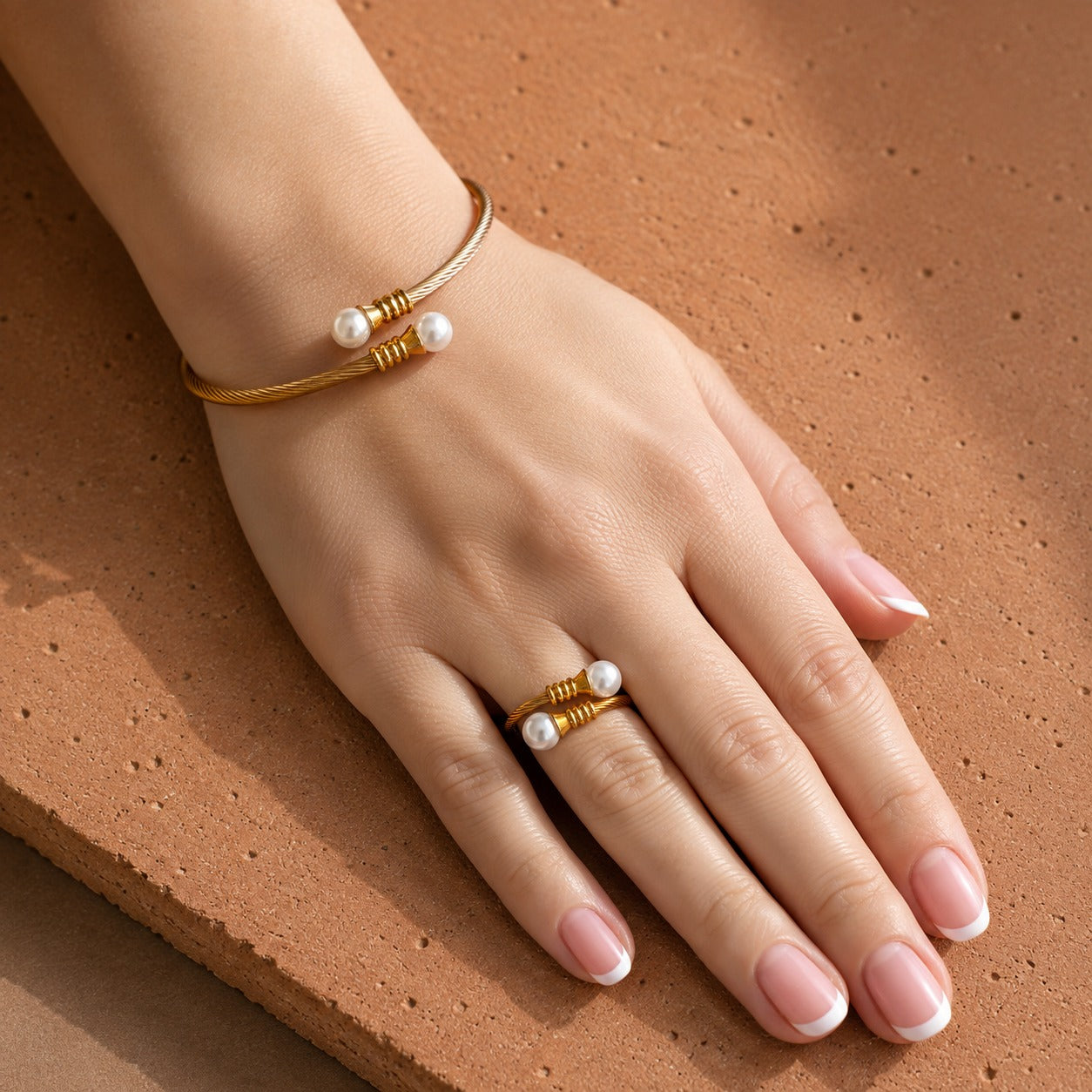 Gold-tone twisted cable bracelet and matching ring with creamy white pearl ends worn together on the hand.