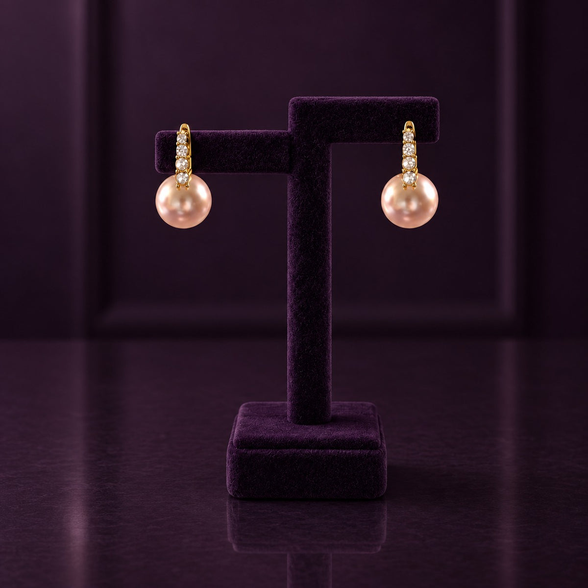 Gold-tone drop earrings with four clear stones and large blush-pink pearl drops displayed on a deep plum jewellery