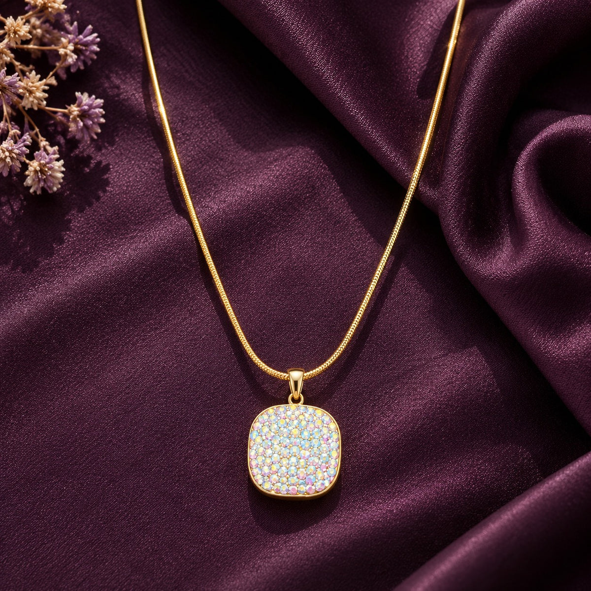 Gold-tone mosaic pendant featuring shimmering multicoloured pastel stones, displayed on rich plum satin fabric with delicate floral accents.