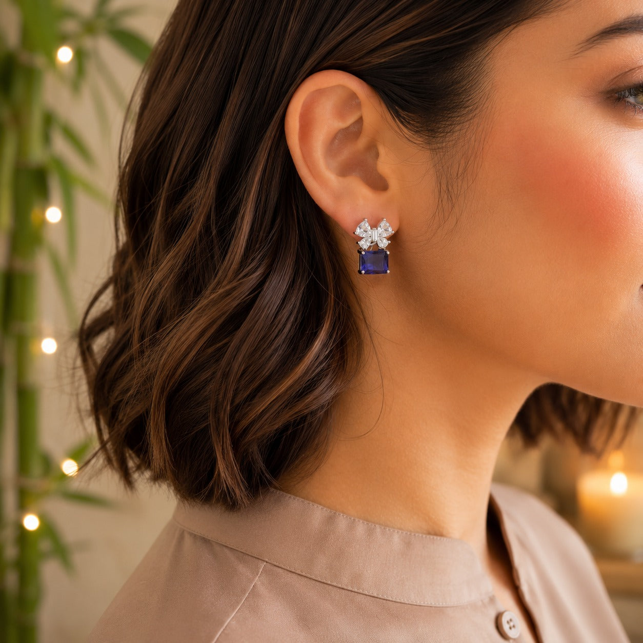 Model wearing floral crystal stud earrings with a sapphire blue emerald-cut gemstone drop.