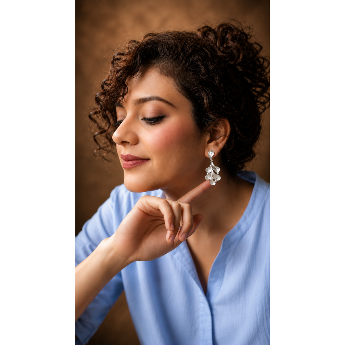 Woman wearing a blue top and floral earrings against a brown background