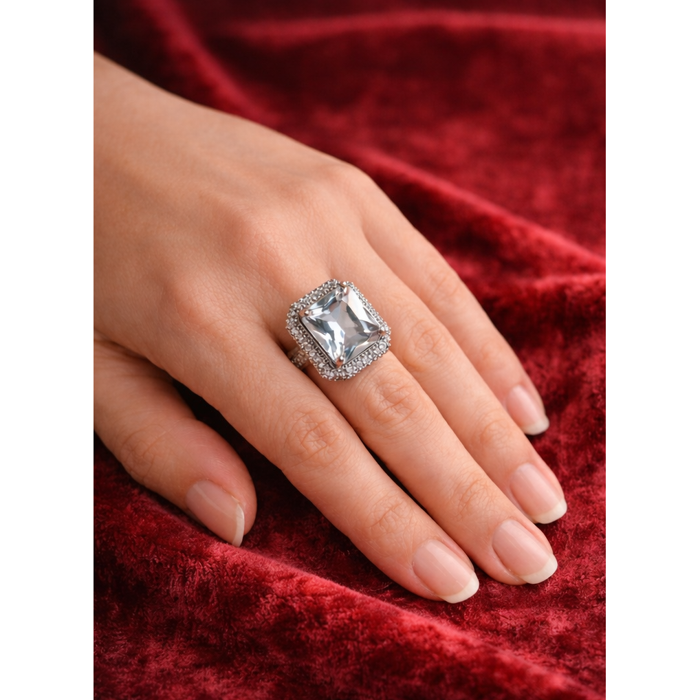 hand wearing an elegant cushion-cut cubic zirconia ring with a double halo of smaller stones resting on red velvet fabric, showcasing a luxury statement jewelry piece.