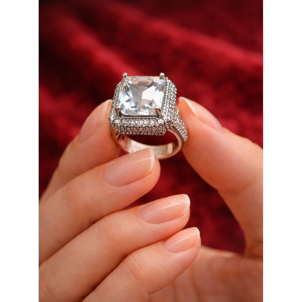 Silver ring with a large central gemstone held by a hand against a red background