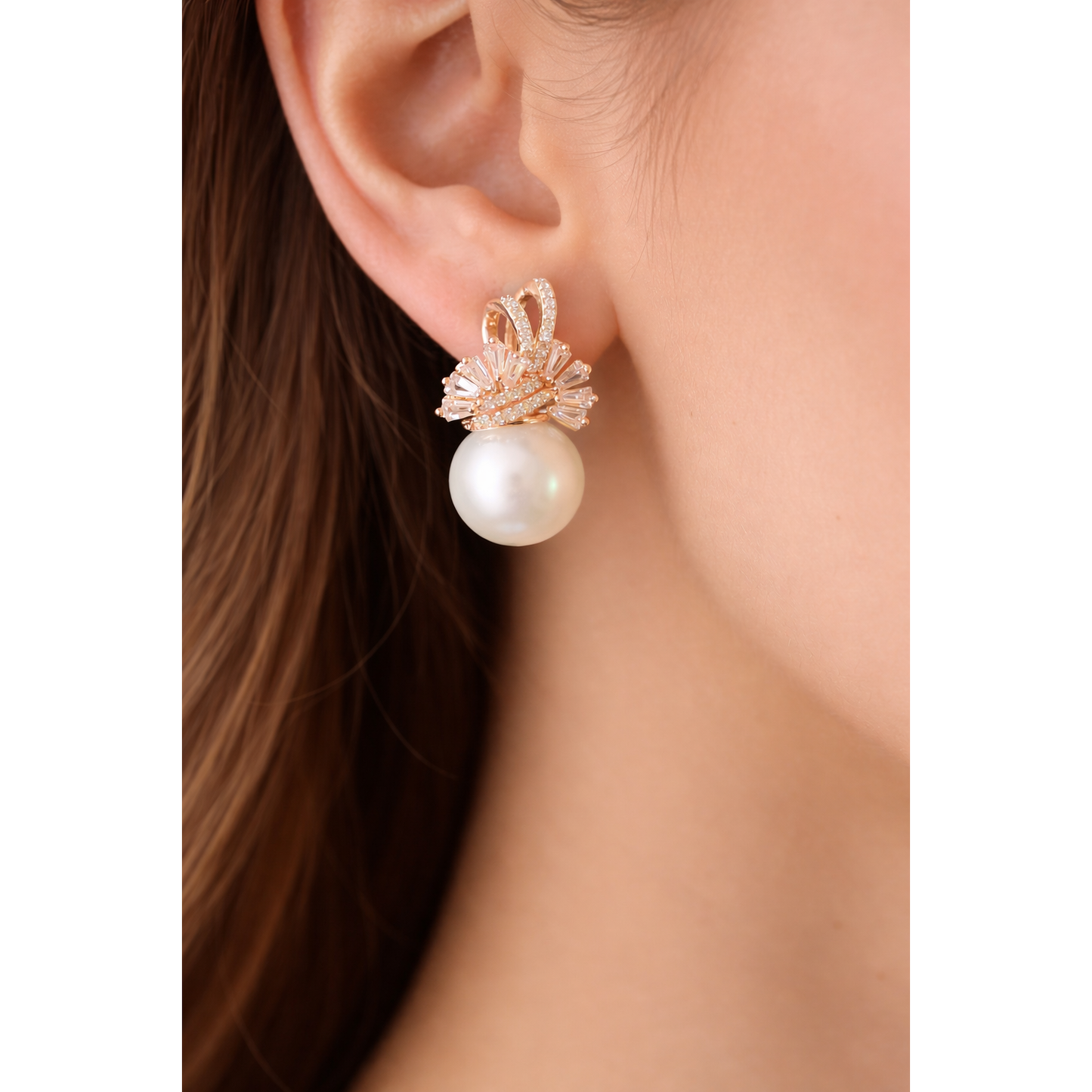 Close-up of TIAS pearl drop earring with crystal design in gold finish worn on ear.