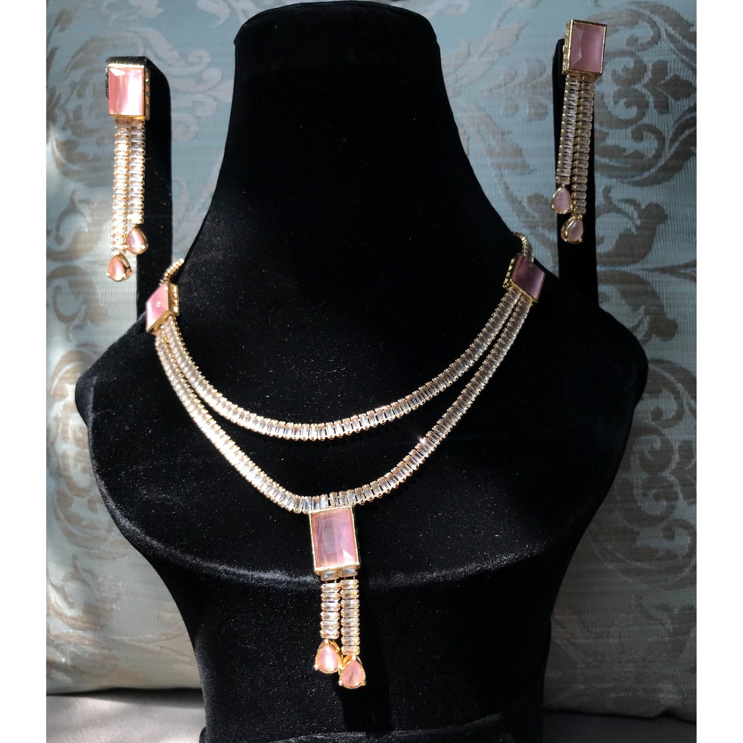 Jewelry set with necklace and earrings on a black mannequin against a decorative wall.