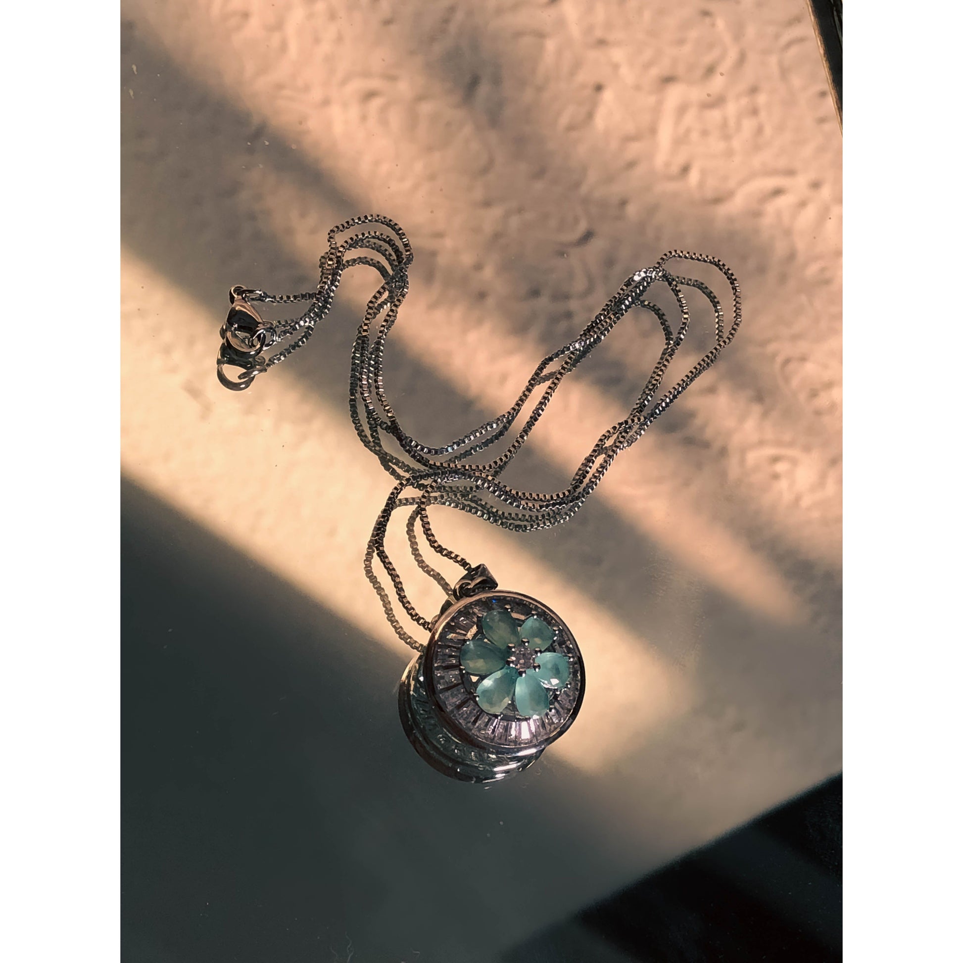 A close-up of a silver-tone necklace with a pendant featuring a clear, flower-shaped cubic zirconia stone surrounded by a halo of smaller clear sparkling stones, on a delicate chain.