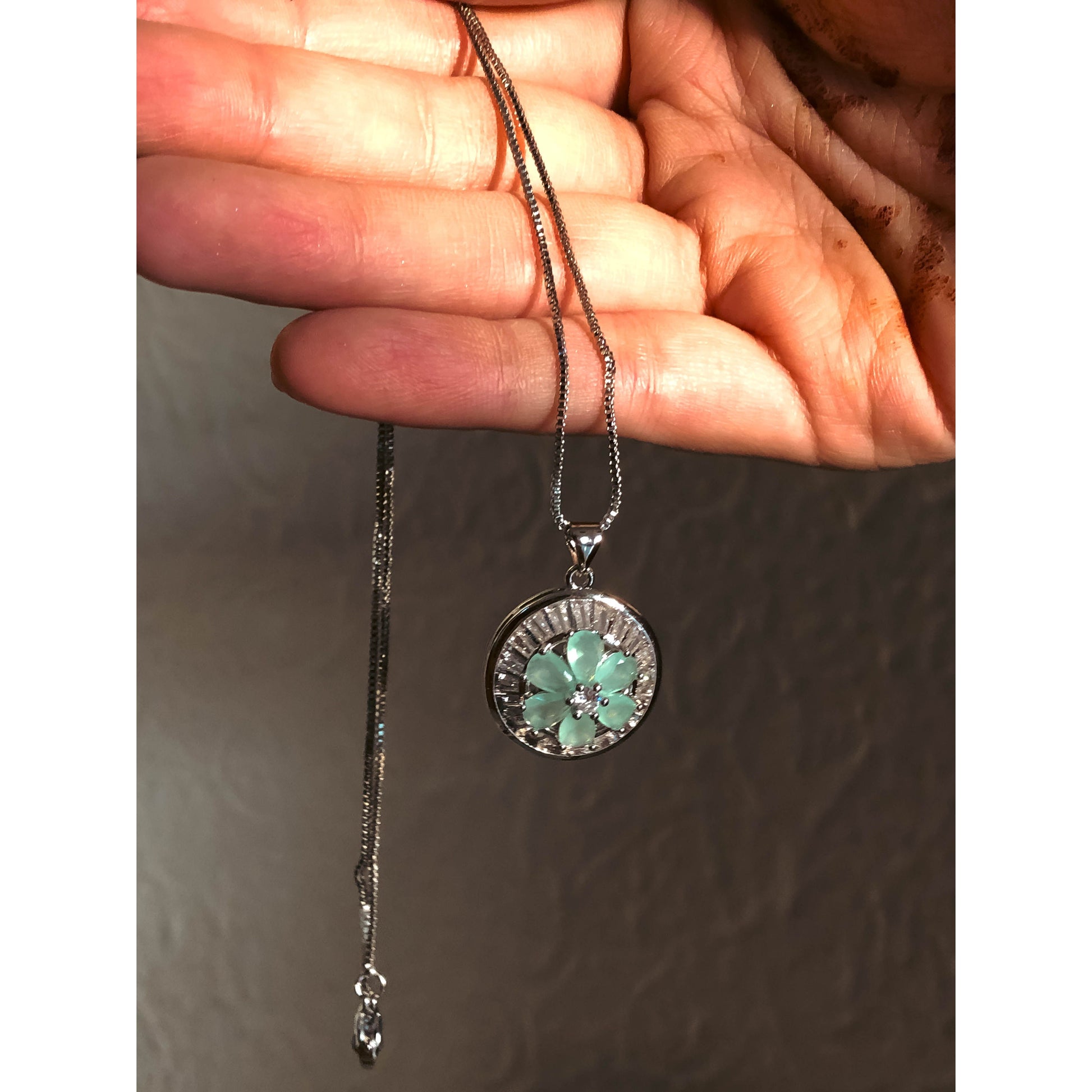 A close-up of a silver-tone necklace with a pendant featuring a clear, flower-shaped cubic zirconia stone surrounded by a halo of smaller clear sparkling stones, on a delicate chain.