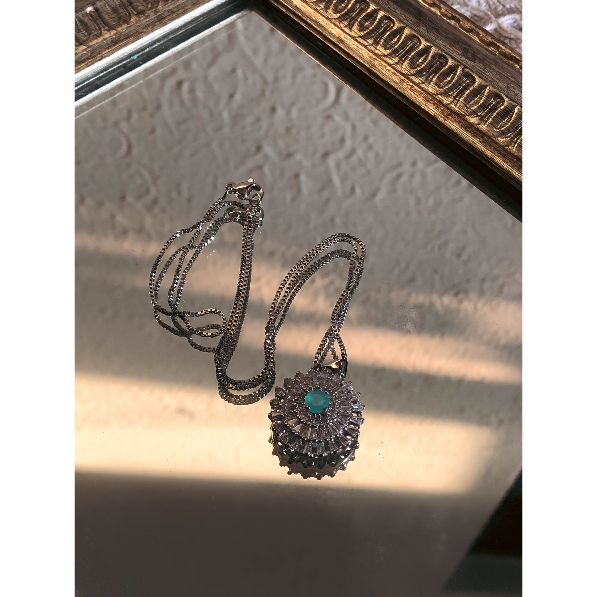 A close-up of a silver-tone necklace with a pendant featuring a large, clear, round stone surrounded by a halo of smaller clear sparkling stones, on a delicate chain.