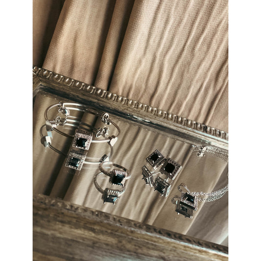 A complete silver-tone jewelry set including a flexible bracelet, a pair of stud earrings, and a necklace with a central pendant, all richly adorned with sparkling clear cubic zirconia stones, displayed on a white background.