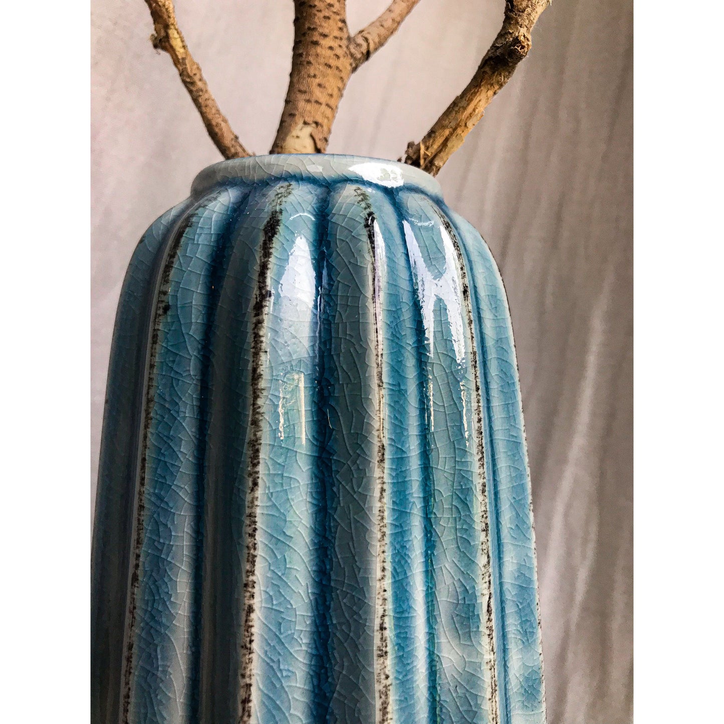 A tall, teal ceramic vase with vertical fluting and a crackled glaze, shown with and without dried branches inside.