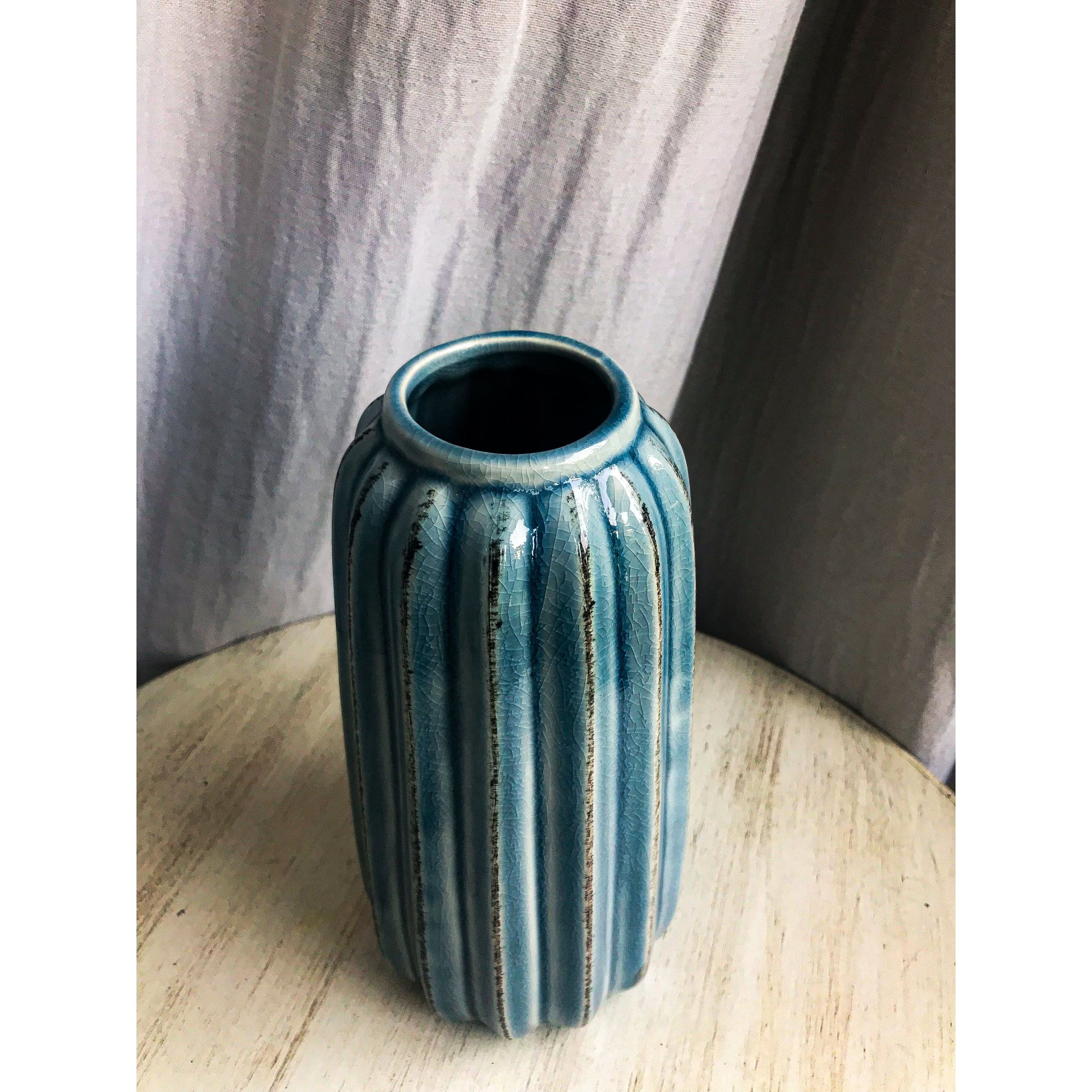 A tall, teal ceramic vase with vertical fluting and a crackled glaze, shown with and without dried branches inside.