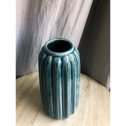 A tall, teal ceramic vase with vertical fluting and a crackled glaze, shown with and without dried branches inside.