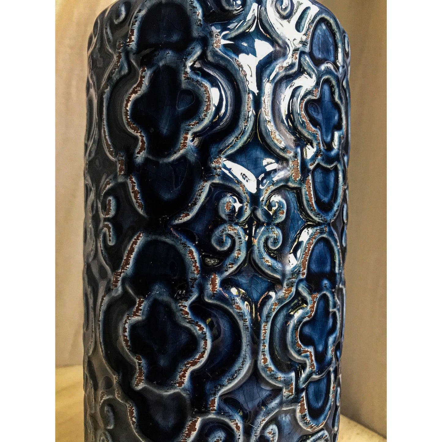 A tall, deep blue ceramic vase with an embossed pattern of quatrefoils and scrolls, shown with and without decorative sticks inside.