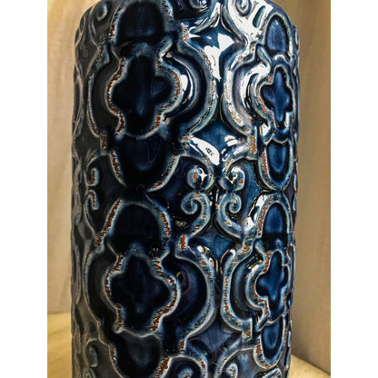 A tall, deep blue ceramic vase with an embossed pattern of quatrefoils and scrolls, shown with and without decorative sticks inside.
