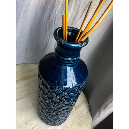 A tall, deep blue ceramic vase with an embossed pattern of quatrefoils and scrolls, shown with and without decorative sticks inside.