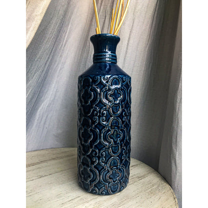 A tall, deep blue ceramic vase with an embossed pattern of quatrefoils and scrolls, shown with and without decorative sticks inside.
