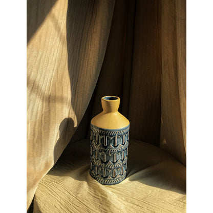 A two-tone ceramic vase with a beige top and a blue bottom featuring an embossed geometric pattern, shown empty and with dried branches.